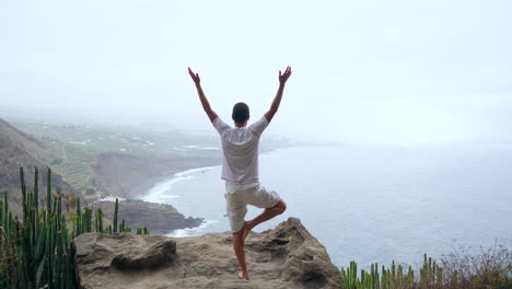 A-youthful-man-performs-sun-salutation-yoga-amidst-mountains-overlooking-the-ocean,-embracing-meditation-and-fitness